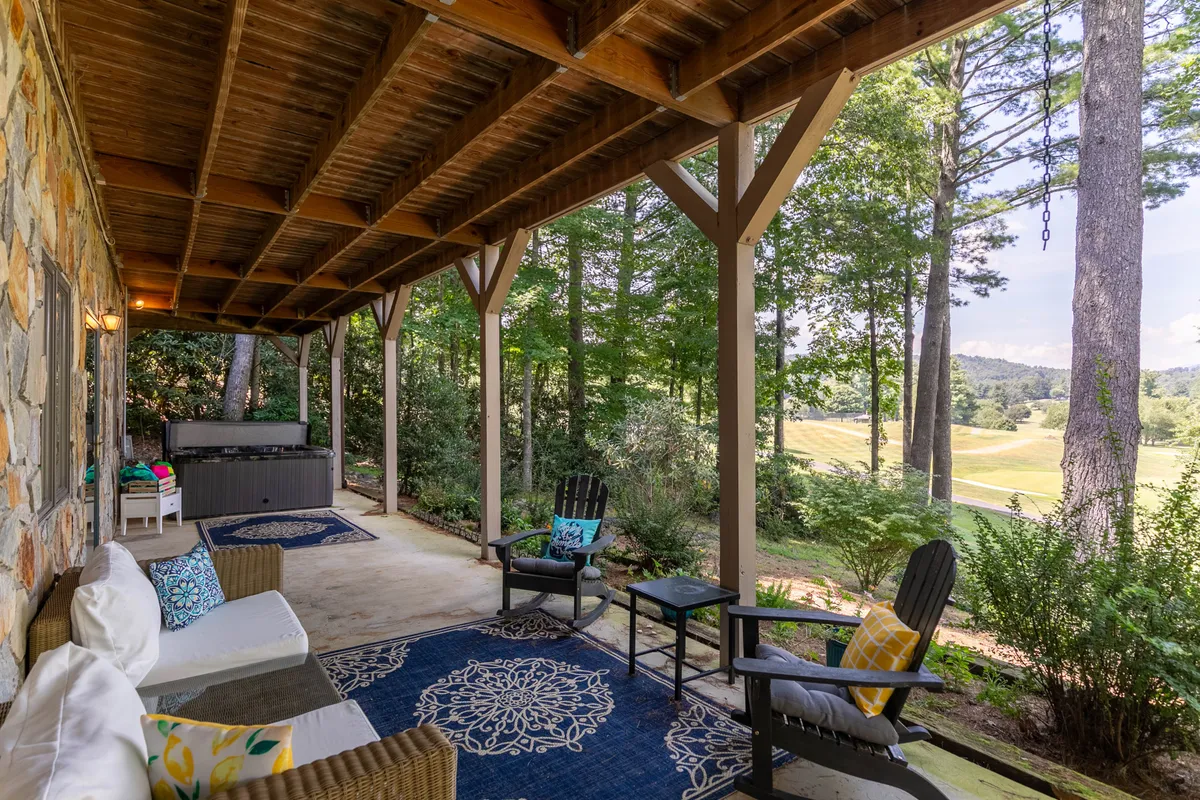 A cozy outdoor seating area with a decorative rug and comfortable chairs is set against a backdrop of lush greenery and distant landscape views. This inviting spot is ideal for relaxing, socializing, or stargazing in peaceful surroundings, capturing the essence of mountain leisure.