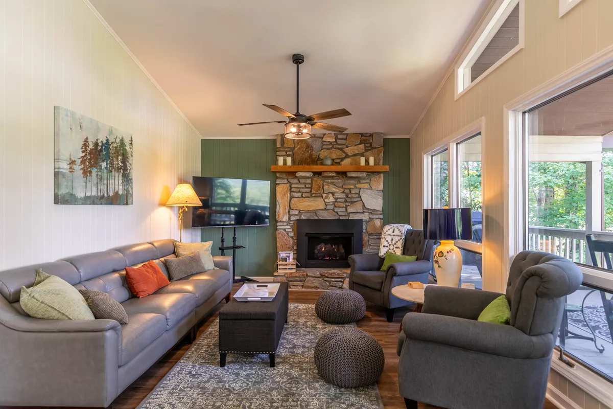 A cozy living room centered around a stone fireplace, with comfortable sofas and a large window letting in mountain light. The atmosphere is perfect for family game nights or relaxing by the fire with loved ones.