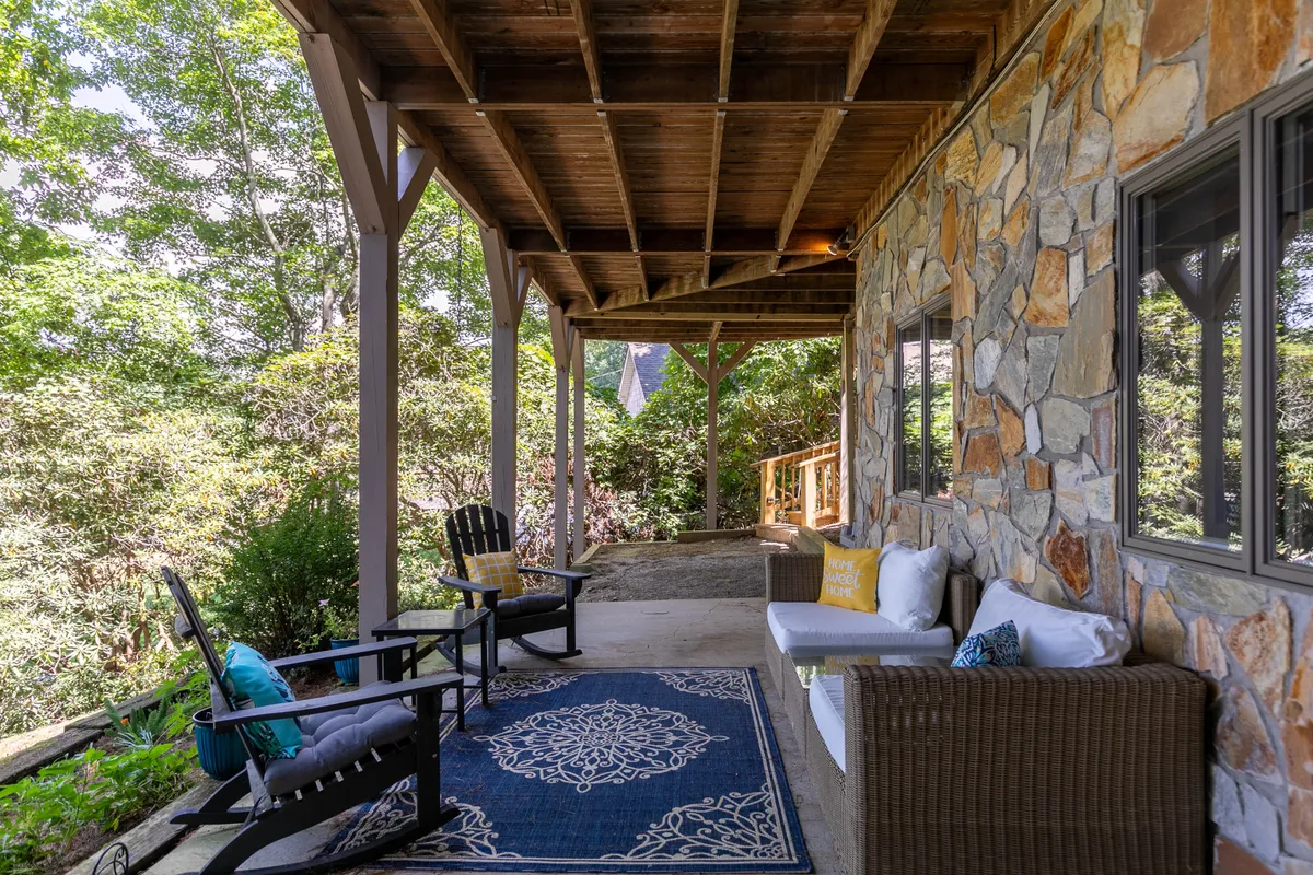 A cozy porch area with rocking chairs, a woven sofa, a decorative rug, and a stone wall set against lush greenery. The setting is ideal for morning coffee, evening chats, or simply soaking in the sunrise and mountain atmosphere.