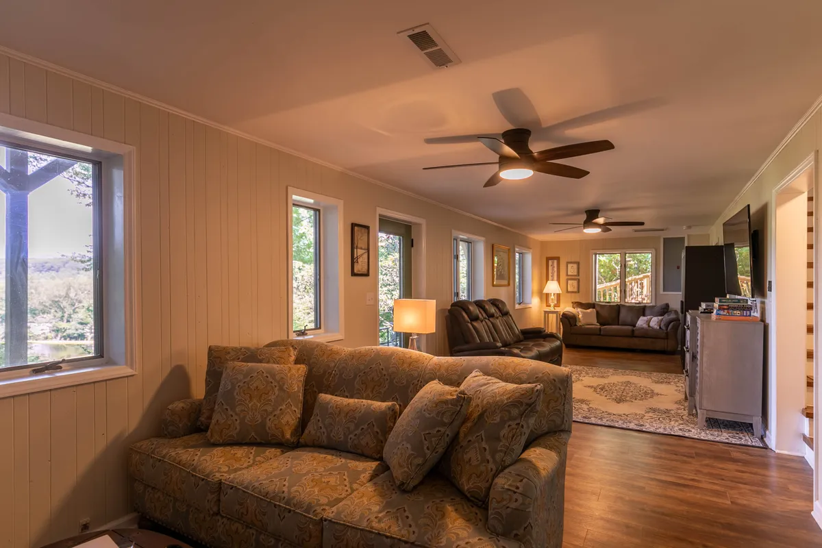 A welcoming living area featuring a patterned sofa, comfortable armchairs, a wooden table, and large windows that flood the space with natural light. The setup suggests a gathering spot for family and friends, with the windows offering views of the outdoors and letting in the changing mountain scenery.