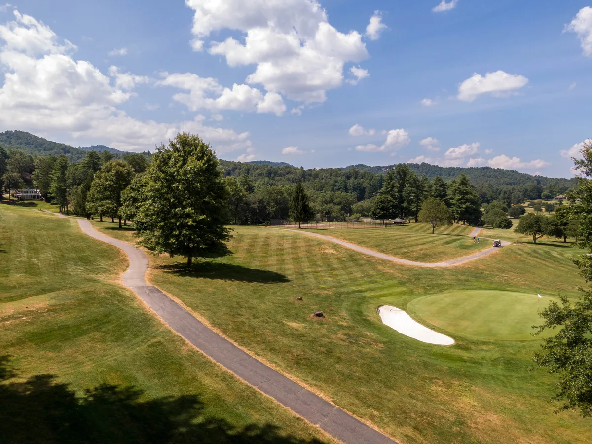 An elevated view showcases the rolling green of a golf course surrounded by trees and hills, with winding pathways that invite exploration. The expansive scenery includes distant mountains, evoking a sense of calm and the promise of outdoor adventure and community activities.