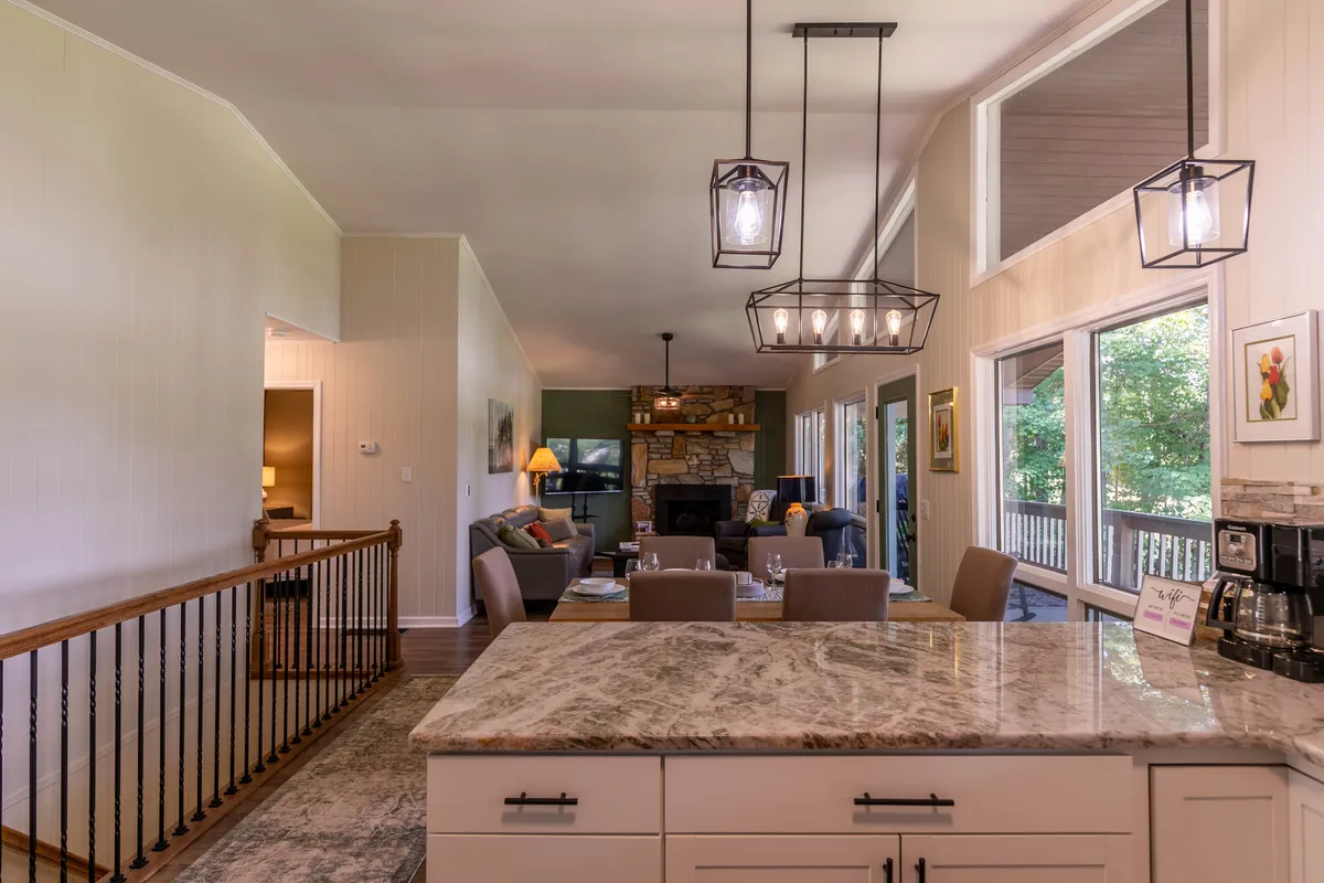 An open-concept kitchen and dining area that flows into the living space, featuring a kitchen island, dining table, and modern appliances. The scene exudes warmth and togetherness, ideal for both cooking and socializing, with views of the living area’s cozy fireplace in the background.