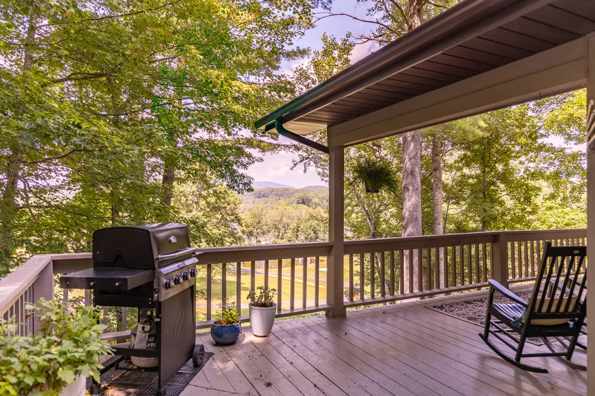 The image depicts a spacious deck featuring a grill, a rocking chair, potted plants, and an open view of the surrounding landscape. The setup suggests a comfortable space for barbecuing, entertaining, and enjoying the fresh air, with warm natural light and inviting decor.