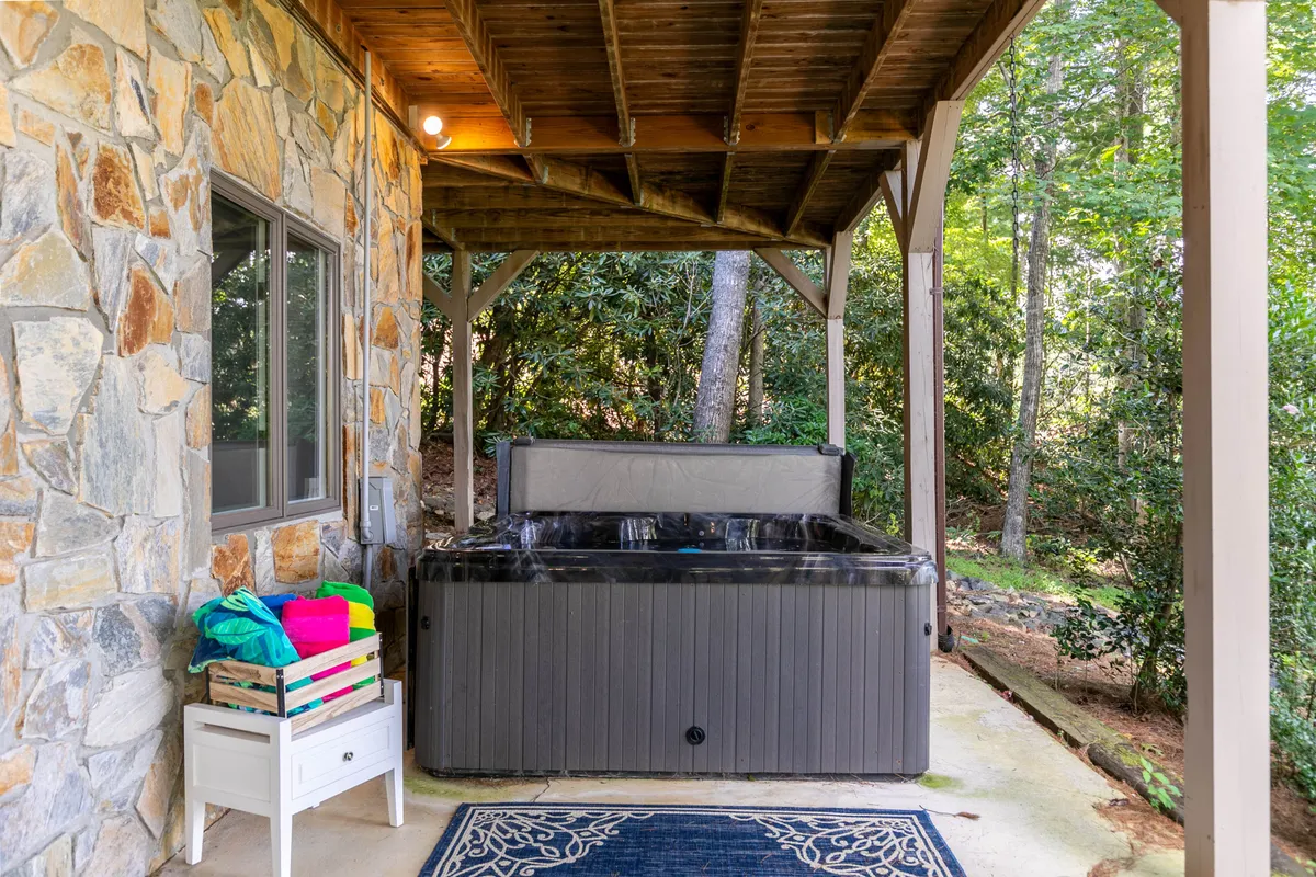 This photo showcases a covered hot tub area bordered by a stone wall and wooden ceiling. The space feels secluded and serene, perfect for stargazing or socializing in any season, with a clear emphasis on comfort and a connection to nature.