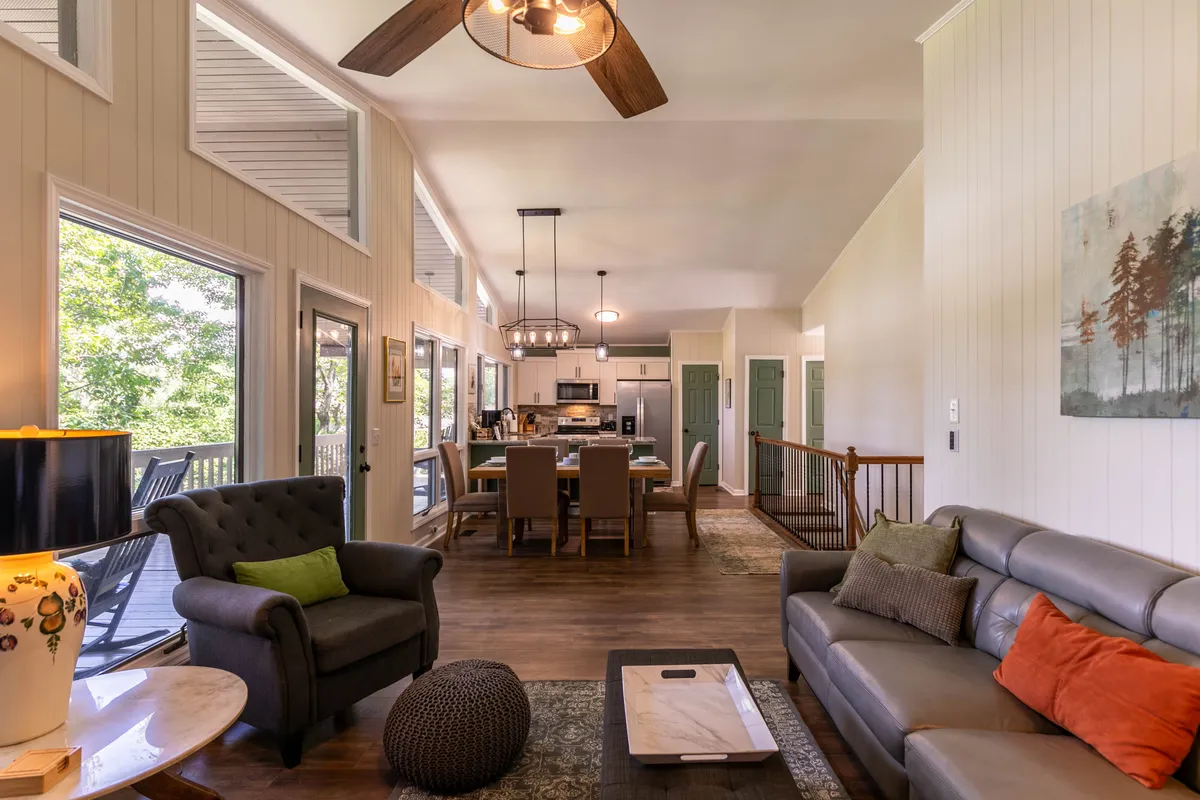 A welcoming, open-concept interior combines a cozy living area with plush seating, a dining table, and a modern kitchen. Large windows flood the space with natural light and offer stunning views outside. The cohesive layout is designed for family gatherings, casual meals, and relaxed evenings.