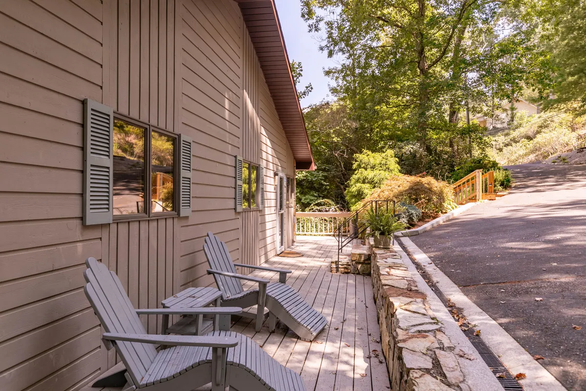 This exterior image features Adirondack chairs set on a wooden deck surrounded by lush greenery, with the cabin's wooden siding visible and a walkway leading through the natural landscape. The scene evokes a sense of tranquility and connection to nature, suggesting a perfect spot for unwinding after exploring local attractions.