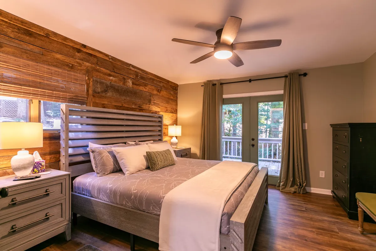 A tranquil, light-filled bedroom with a cozy bed framed by a wooden accent wall and a window revealing glimpses of nature outside. The space invites relaxation and quiet moments, suggesting a peaceful retreat after a day of travel and exploration.